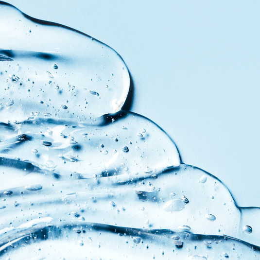 Clear gel texture with small bubbles spread on a light blue background, representing the moisturizing and soothing qualities of Eye Gel 28mL | Hommage skincare product.