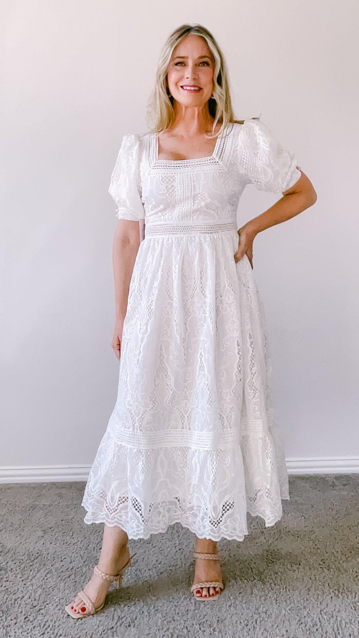 Woman wearing white lace midi dress with puff sleeves and square neckline, paired with nude heeled sandals