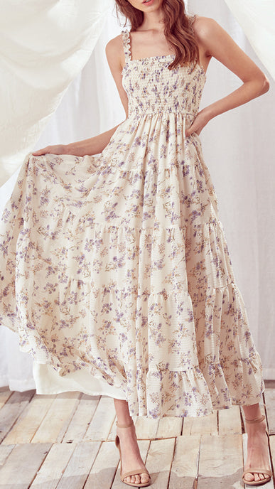 Woman wearing a cream floral smocked maxi dress with ruffled straps and beige heels in bright indoor setting