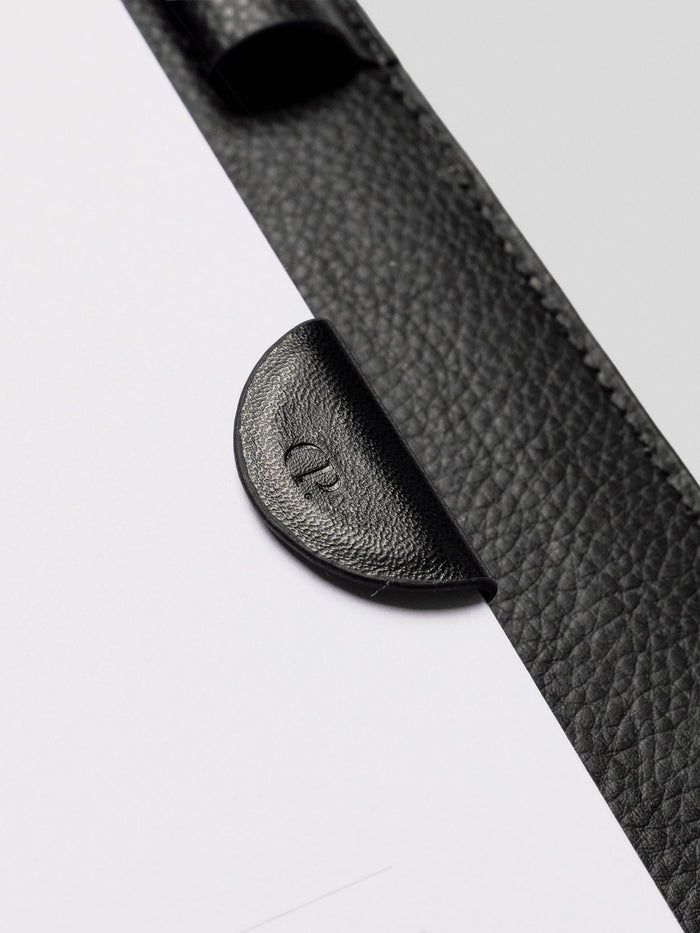 Close-up of the black leather magnetic bookmark clipped onto the edge of a planner page with a black leather cover.