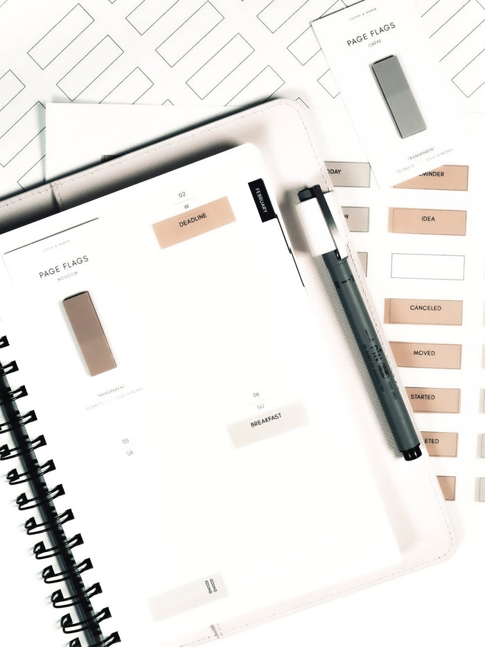 Page Flag Printable | Admin printable page layered underneath a planner with page flags in use inside it. Page flags on their backings are layered on top of the planner and printable pages.